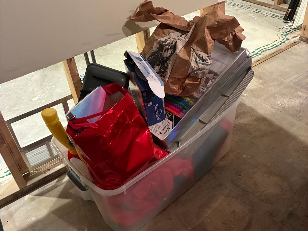 Plastic storage bin full of gift bags and craft supplies in a Clarendon Hills basement with drywall cut away during a remodel