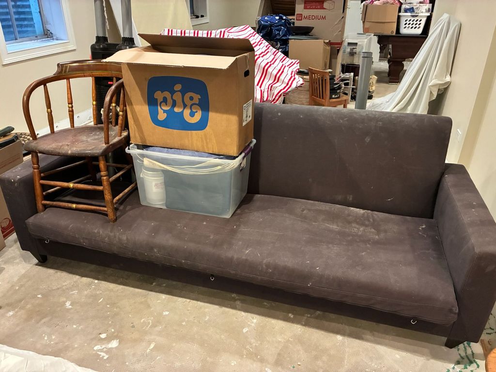 Old couch in a Clarendon Hills basement with a wooden chair, cardboard box and storage bin stacked on it before junk removal