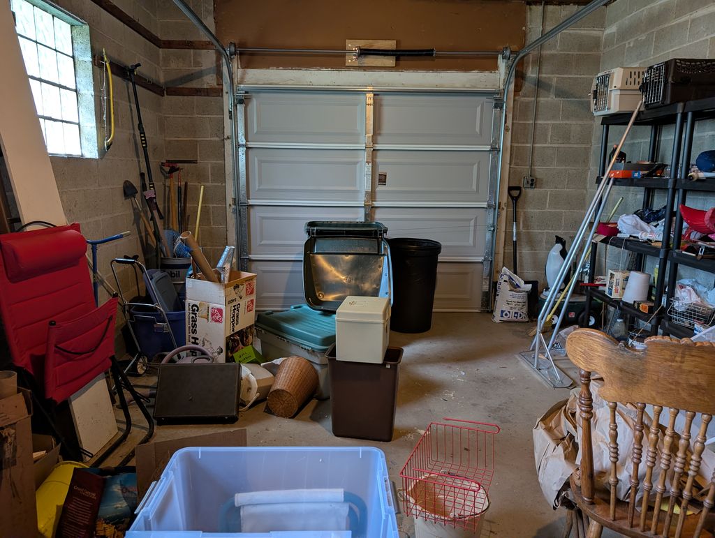 Cluttered one-car garage in Mundelein before a garage clean-out, with storage bins, trash cans, garden tools and shelving