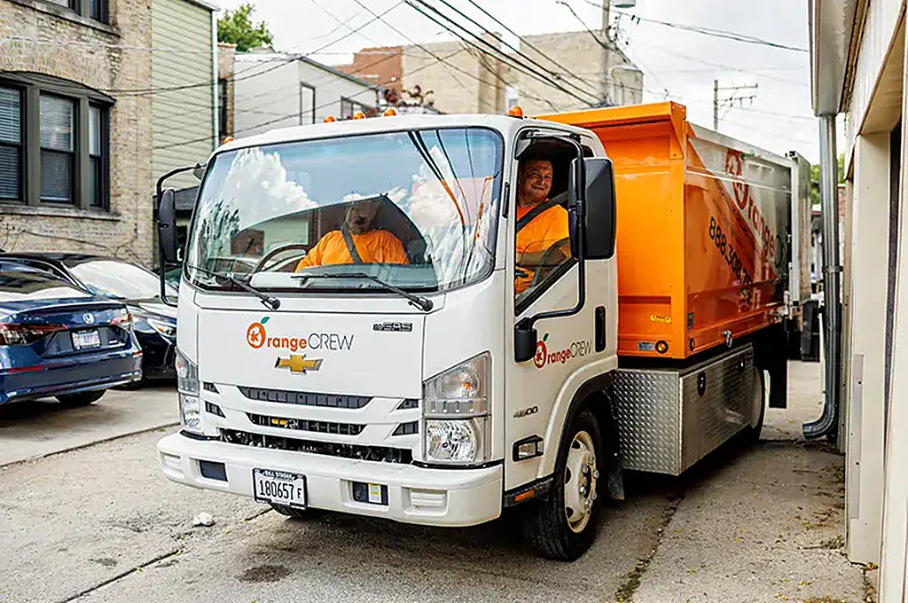 Orange Crew junk removal truck loading yard waste in a Chicago neighborhood